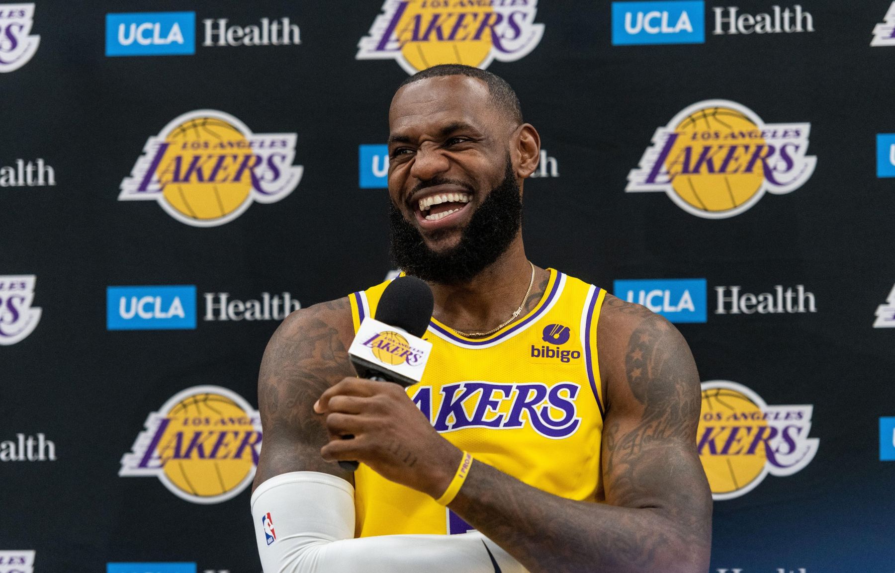 Basketball star laughing at a media day in front of a sponsor backdrop